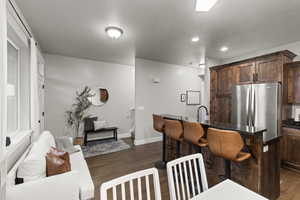 Kitchen featuring dark wood-style flooring, a kitchen bar, freestanding refrigerator, recessed lighting, and dark stone counters