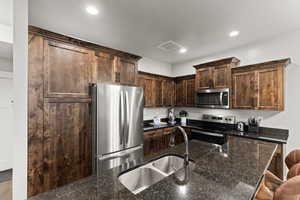 Kitchen featuring stainless steel appliances, dark brown cabinetry, recessed lighting, a breakfast bar area, and dark stone counters