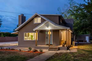 View of front facade with covered porch, a chimney, and stucco siding
