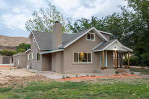 View of front facade featuring a chimney, a shingled roof, stucco siding, a front lawn, and a porch