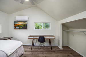 Bedroom with dark wood finished floors, a wall mounted air conditioner, lofted ceiling, ceiling fan, and an office area