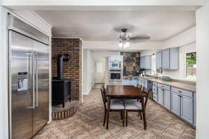 Kitchen with built in appliances, light countertops, gray cabinets, a wood stove, and a ceiling fan