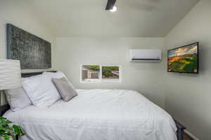 Bedroom with a wall unit AC, ceiling fan, and lofted ceiling