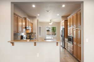Kitchen featuring brown cabinets, recessed lighting, a peninsula, light stone counters, and a kitchen breakfast bar