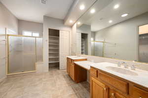 Bathroom with a walk in closet, a shower stall, two vanities, recessed lighting, and light tile patterned floors