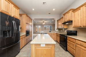 Kitchen with black appliances, light stone countertops, recessed lighting, a center island, and under cabinet range hood
