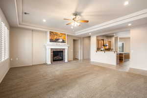 Unfurnished living room featuring light colored carpet, ceiling fan, a raised ceiling, recessed lighting, and a brick fireplace