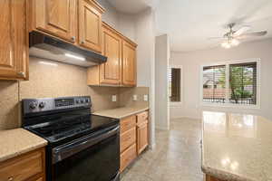 Kitchen featuring black / electric stove, under cabinet range hood, light stone countertops, and tasteful backsplash
