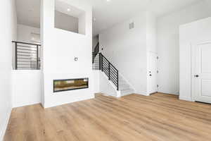 Unfurnished living room with stairway, light wood-style floors, a glass covered fireplace, and recessed lighting