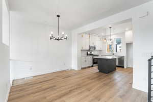 Kitchen with white cabinets, appliances with stainless steel finishes, a chandelier, pendant lighting, and light wood finished floors