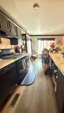 Kitchen featuring black appliances, dark wood finished floors, light countertops, under cabinet range hood, and dark brown cabinets