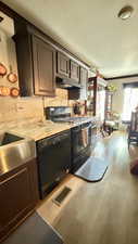 Kitchen featuring black appliances, dark brown cabinetry, light countertops, under cabinet range hood, and light wood-style floors