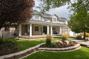 View of front of house with a front lawn, brick siding, a porch, a garage, and a shingled roof