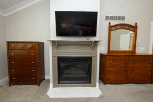 Living room featuring light carpet, a glass covered fireplace, and ornamental molding