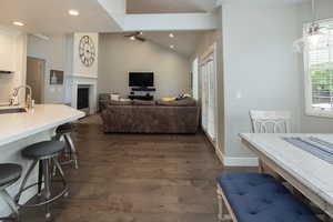 Dining room featuring a ceiling fan, healthy amount of natural light, lofted ceiling, a fireplace, and dark wood-style flooring