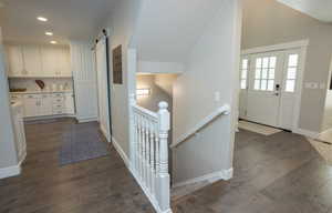 Hallway featuring a barn door, an upstairs landing, dark wood-type flooring, recessed lighting, and vaulted ceiling