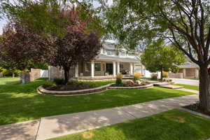 View of property hidden behind natural elements with covered porch, brick siding, and a front yard