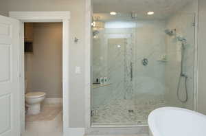Bathroom featuring light marble finish flooring, a marble finish shower, and a freestanding tub