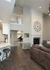 Living room featuring recessed lighting, dark wood-style flooring, a glass covered fireplace, and a towering ceiling