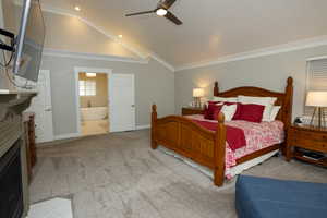 Carpeted bedroom featuring ornamental molding, a fireplace, high vaulted ceiling, a ceiling fan, and connected bathroom