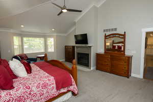 Bedroom featuring high vaulted ceiling, a fireplace with flush hearth, light colored carpet, ceiling fan, and ornamental molding