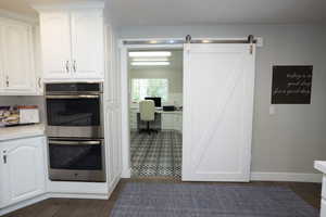 Kitchen with stainless steel double oven, white cabinetry, backsplash, dark wood finished floors, and a desk