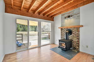 Unfurnished living room with a wood stove, a wood ceiling with exposed beams, and light wood-style flooring