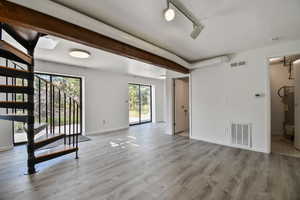 Unfurnished living room with light wood finished floors, beam ceiling, track lighting, stairs, and water heater