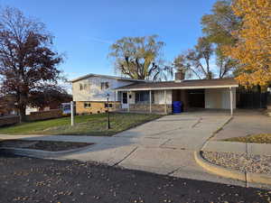 Tri-level home with concrete driveway, brick siding, a chimney, and an attached carport