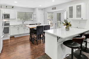 Kitchen featuring a kitchen bar, backsplash, white cabinetry, light stone countertops, and glass insert cabinets
