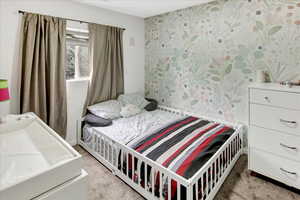 Bedroom with light colored carpet, wallpapered walls, and washer / dryer