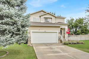 Traditional-style house with concrete driveway, a garage, a front lawn, and roof with shingles