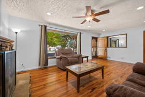 Living room featuring wood finished floors, a textured ceiling, ceiling fan, recessed lighting, and a fireplace