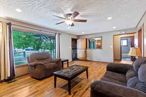 Living area featuring light wood-type flooring, ceiling fan, a textured ceiling, and recessed lighting