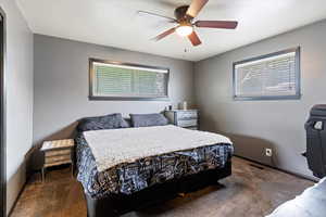 Bedroom with dark carpet, multiple windows, and ceiling fan