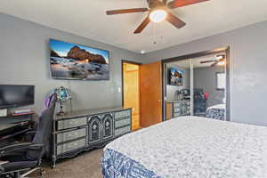Bedroom with dark colored carpet, a ceiling fan, a desk, and a closet