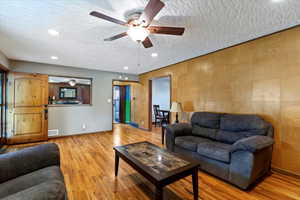 Living area with wood finished floors, a ceiling fan, a textured ceiling, and recessed lighting
