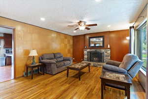 Living area featuring a ceiling fan, a stone fireplace, wood finished floors, a textured ceiling, and recessed lighting