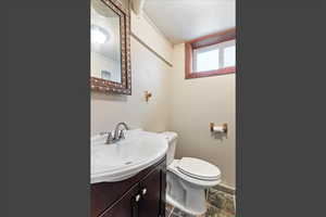 Half bathroom with vanity, ornamental molding, and stone finish flooring