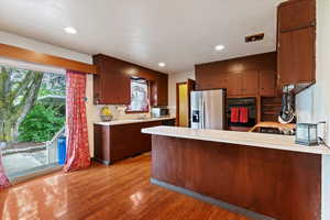 Kitchen with a peninsula, light countertops, stainless steel appliances, dark wood finished floors, and recessed lighting