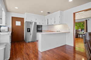 Kitchen featuring a peninsula, light countertops, white cabinetry, stainless steel fridge with ice dispenser, and decorative backsplash