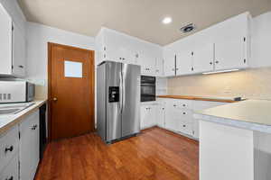 Kitchen featuring black appliances, dark wood finished floors, white cabinetry, decorative backsplash, and light countertops
