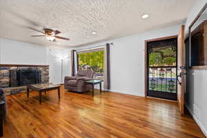 Living area featuring a textured ceiling, a stone fireplace, light wood-style flooring, recessed lighting, and ceiling fan