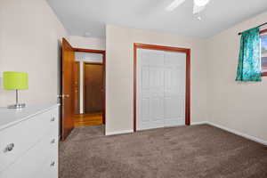 Unfurnished bedroom with dark carpet, a closet, and a ceiling fan