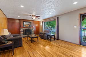 Living room with a ceiling fan, light wood-type flooring, wood walls, recessed lighting, and a stone fireplace