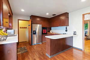 Kitchen with stainless steel fridge, a peninsula, light countertops, dark wood finished floors, and recessed lighting