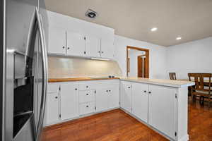 Kitchen featuring stainless steel refrigerator with ice dispenser, a peninsula, white cabinetry, tasteful backsplash, and dark wood-style flooring