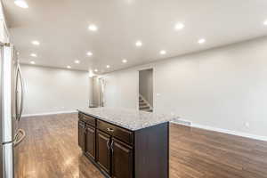 Kitchen featuring dark brown cabinetry, recessed lighting, dark wood finished floors, freestanding refrigerator, and light stone countertops