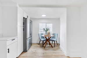 Kitchen with white cabinetry, freestanding refrigerator, light wood-style floors, and light stone counters