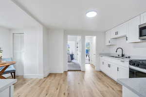 Kitchen featuring white cabinetry, light wood-type flooring, light stone countertops, and stainless steel microwave